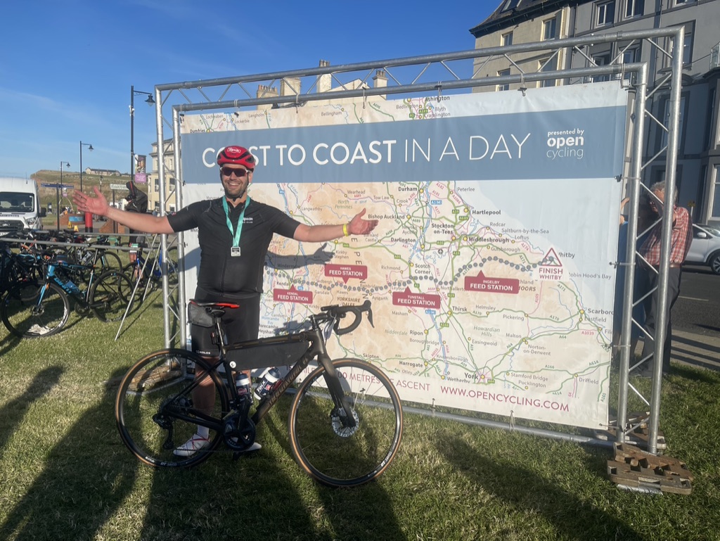 Wielrenner poseert met zijn racefiets bij het finishbord van de fietstocht ‘Coast to Coast in a Day’